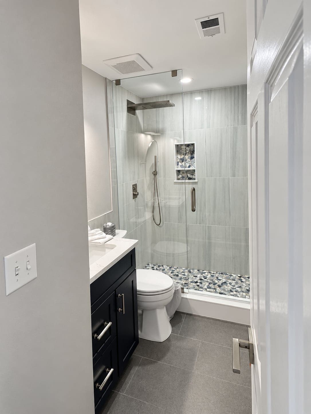 Condo bathroom with a glass shower, a pebble floor, a navy vanity and a new floor