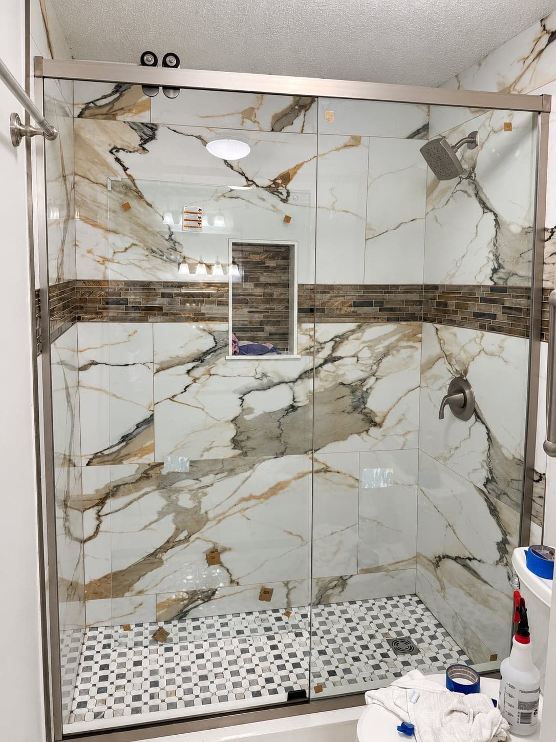 Walk-in shower finished in marble-look tile with a mosaic band, a niche and a glass door