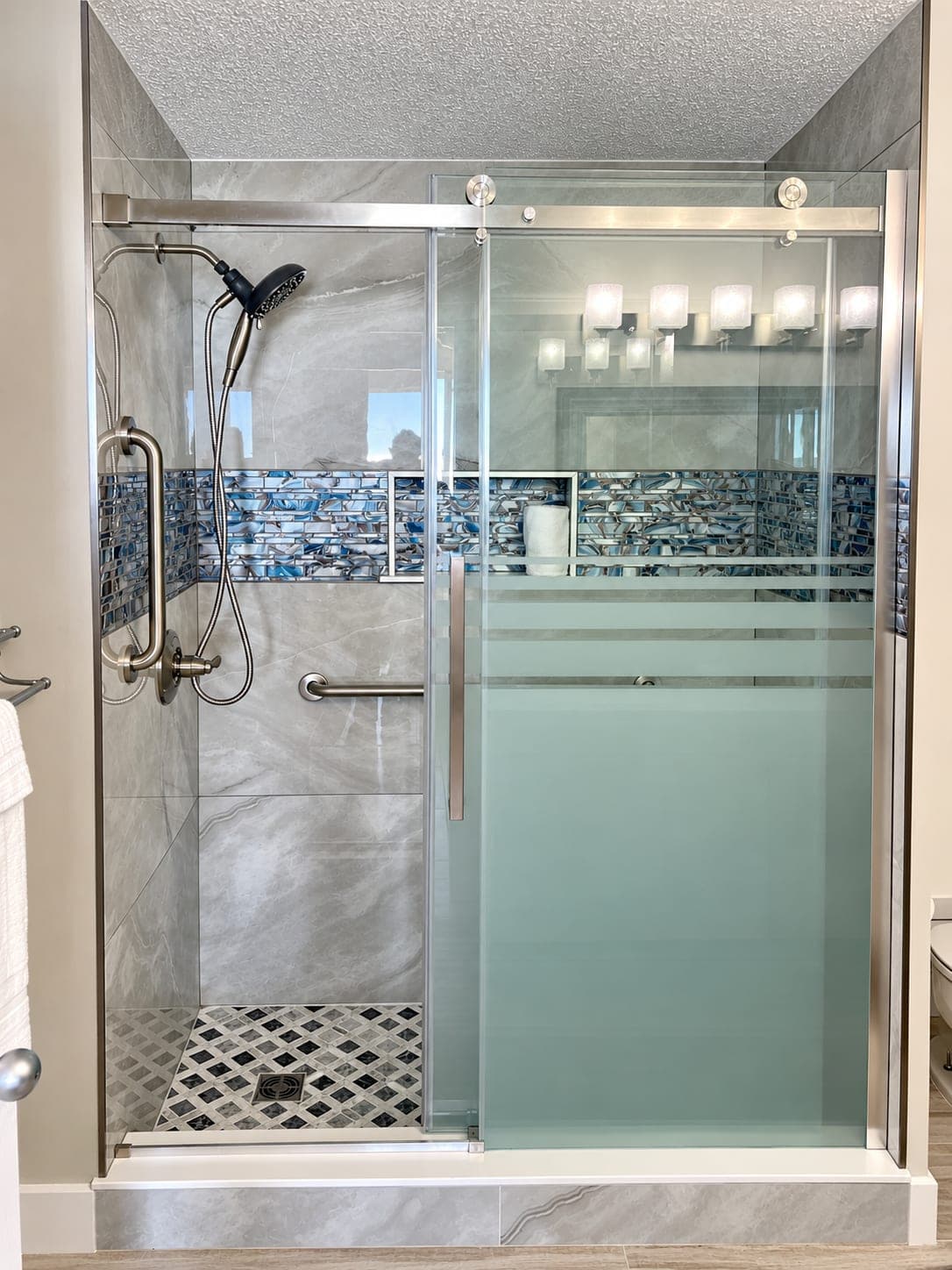 Walk-in shower with a glass door, large-format tile and a blue mosaic band