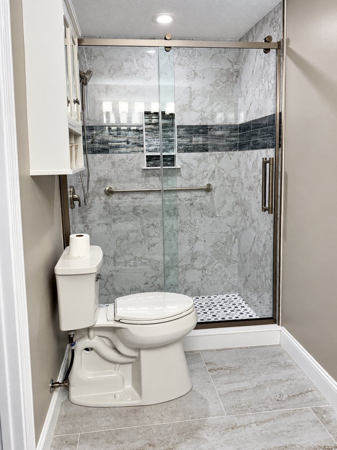 Condo bathroom finished with a marble-look shower, a mosaic band and a glass door