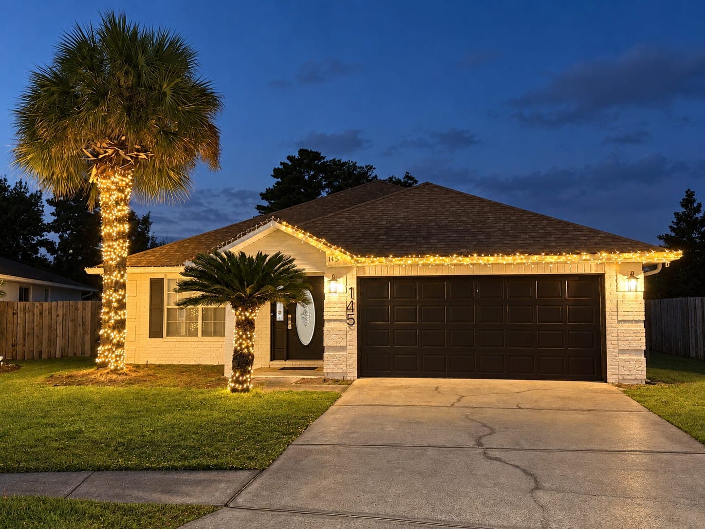 Single-story house repainted white with a dark garage door, photographed at night with the lights on