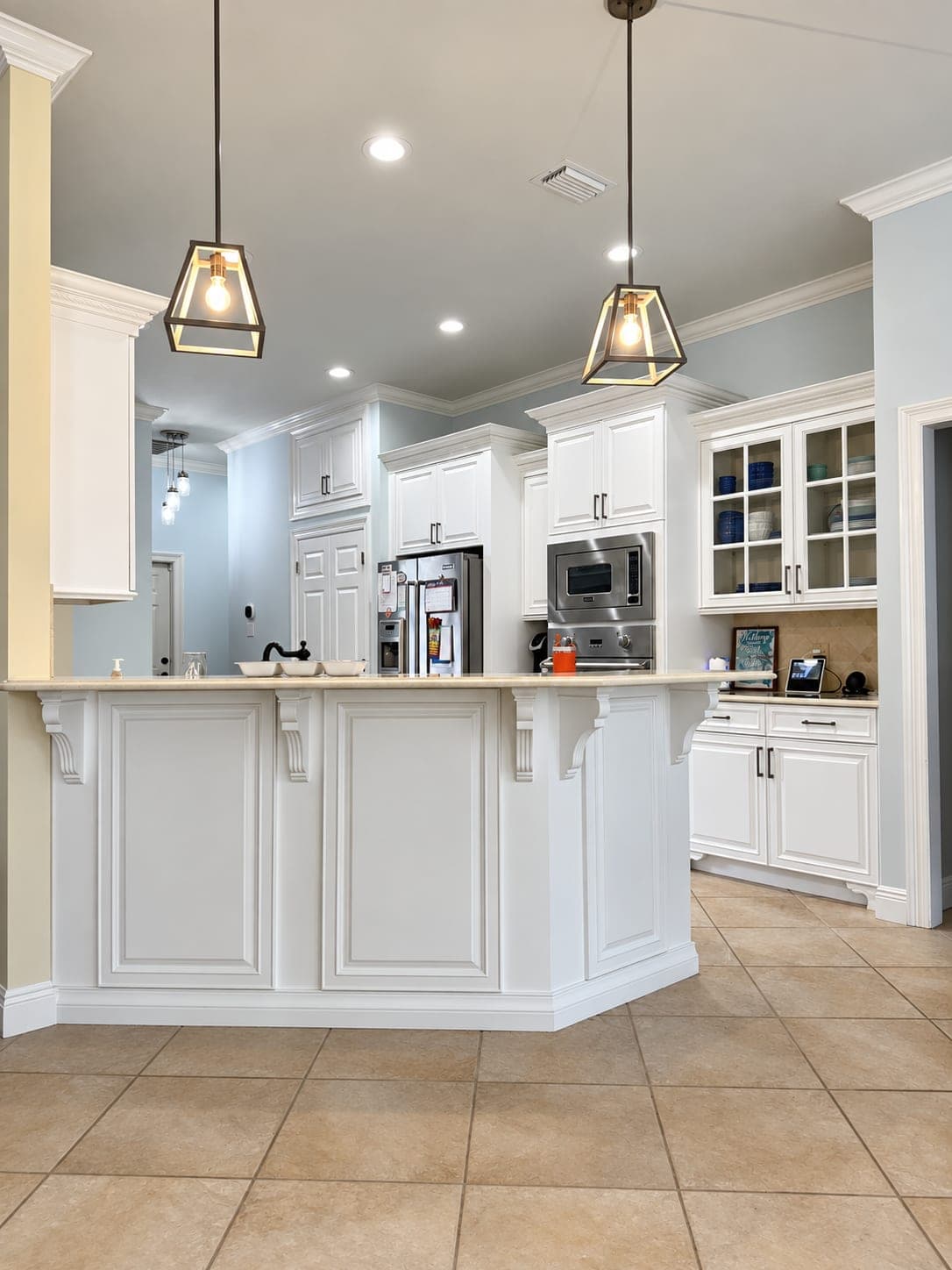 White kitchen with an island, pendant lights and a dining area after a cabinet and backsplash update