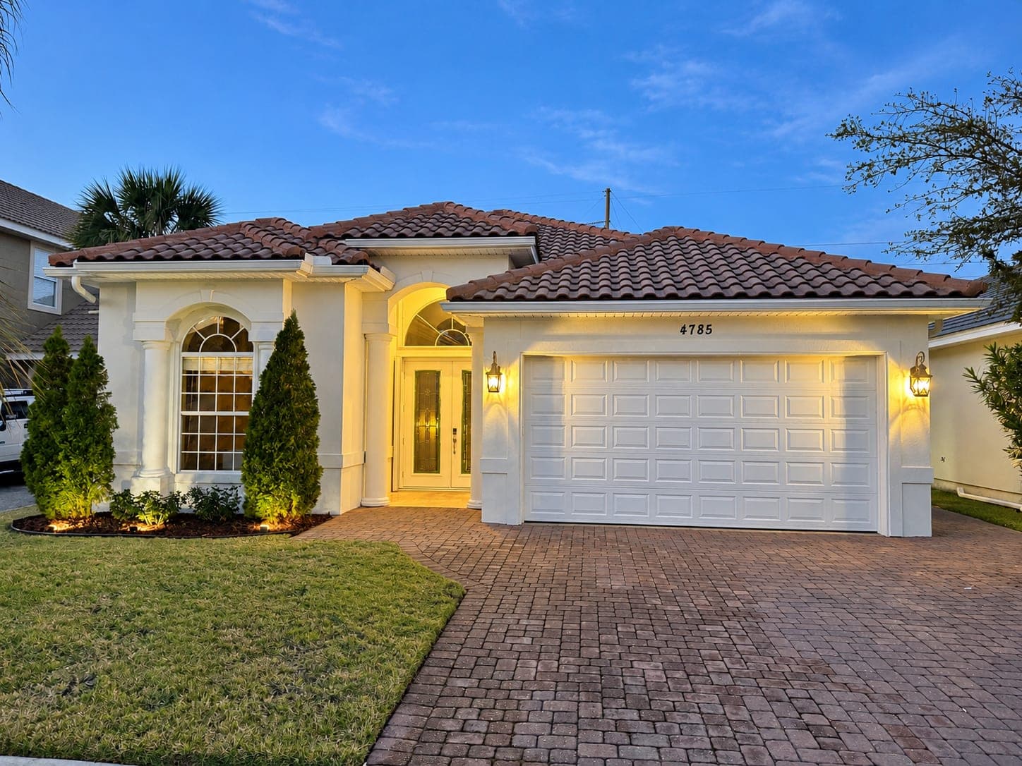 Stucco house with a tile roof and paver driveway, freshly painted and lit at dusk