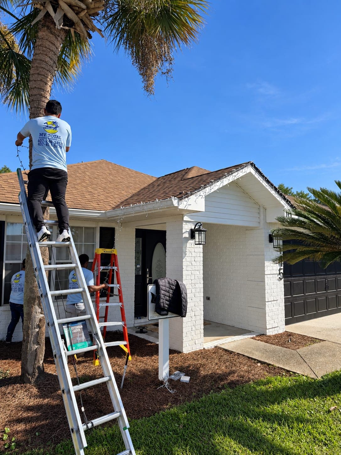 Two members of the MV team working on the front of a freshly painted white house, one on a ladder